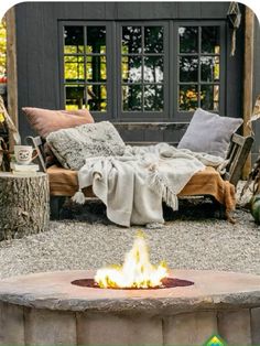 a fire pit in the middle of a gravel area with pillows and blankets on it