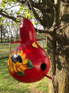 a red birdhouse hanging from a tree with sunflowers painted on it's side