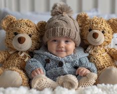 a baby sitting between two teddy bears in a crocheted outfit and knitted hat