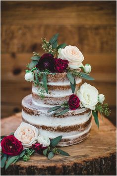 a three tiered cake with flowers and greenery sits on top of a tree stump