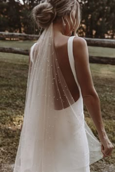 the back of a woman wearing a wedding dress with pearls on it and a veil over her head