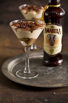 two glasses filled with dessert sitting on top of a metal tray next to a bottle