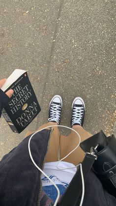 someone is holding a book and some shoes on the ground with their feet propped up in front of them