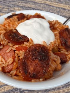 a white plate topped with rice and sausage covered in sour cream next to a fork