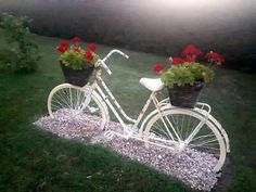 a white bicycle with flowers in the basket is sitting on some gravel and grass outside