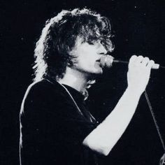 a man with long hair holding a microphone in his hand and singing into the microphone