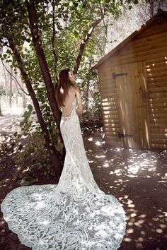 a woman standing in front of a tree wearing a white wedding dress with open back