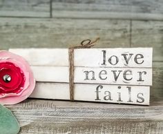 a wooden sign that says love never falls with a pink flower on the front and side