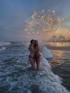 two women are hugging in the ocean with fireworks coming out of their heads and buildings in the background