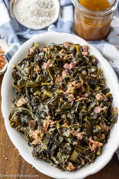 a white bowl filled with collard greens next to two bowls of rice and seasoning