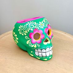 a green skull with pink flowers painted on it's face sitting on a table