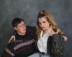 a man sitting next to a woman on top of a chair in front of a wall