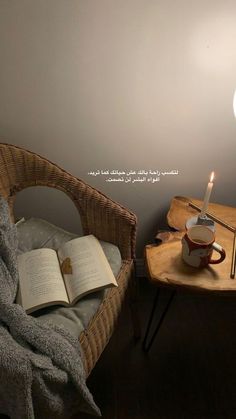 an open book sitting on top of a wooden table next to a lit candle in a cup