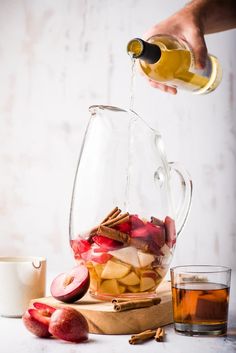 someone pouring apple cider into a pitcher filled with apples