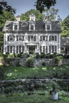 a large white house sitting in the middle of a lush green field with lots of trees