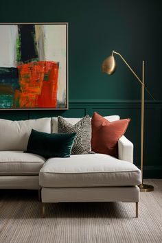 a living room with green walls, white couch and gold floor lamp in the corner