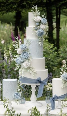 a wedding cake with blue flowers and greenery on the top is surrounded by candles