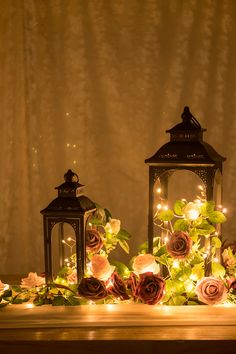 two lanterns with roses and fairy lights on them