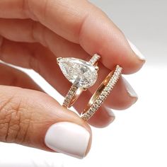 a woman's hand holding an engagement ring and wedding band with a pear shaped diamond