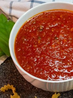 a white bowl filled with red sauce next to green leaves and star shaped cookies on a table