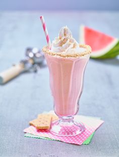 a milkshake with whipped cream and graham crackers on a table next to a slice of watermelon