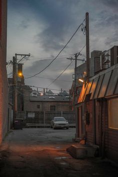 an alley way with cars parked on the side and power lines above it at dusk