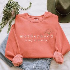 "Motherhood is a gift from above. This terracotta Comfort Colors sweatshirt features a minimalistic boho style graphic of the text \"motherhood is my ministry\" and a green flower. With A Wildflower aims to blend faith and fashion, focusing on minimalist and boho styles. Comfort Colors sweatshirts are super soft and super comfy, featuring garment-dyed 80% ring-spun cotton and 20% polyester. Each sweatshirt comes with a relaxed unisex fit, a rolled-forward shoulder, and a back neck patch.  It wil Motherhood Is My Ministry, Mom Cricut Shirts, Stay At Home Mom Aesthetic, Christian Mom Gifts, Minimalistic Boho, Homeschool Shirts, Text Graphic, Comfort Colors Sweatshirt