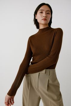 a woman is wearing a brown turtle neck sweater and khaki pants with her hands on her hips