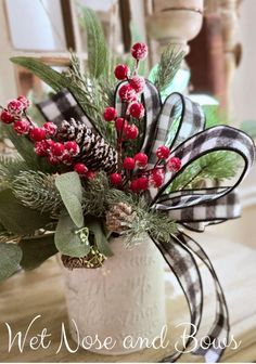 a white vase filled with red berries and pine cones on top of a wooden table