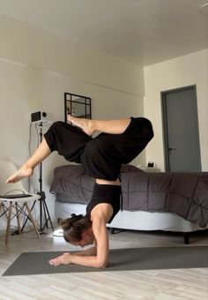 a woman is doing a handstand on her yoga mat in the middle of a bedroom