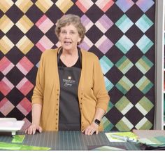 an older woman standing in front of a quilt