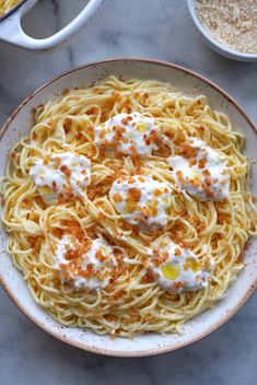 a white bowl filled with pasta covered in cheese and sauce on top of a marble table