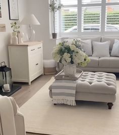 a living room with white furniture and flowers in vases on the coffee table next to the couch