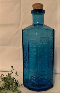 a blue glass bottle with a corked top sitting next to a small green plant