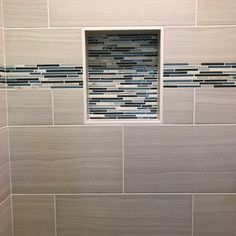 a white tiled bathroom with blue and gray glass mosaics on the shower wall next to the toilet