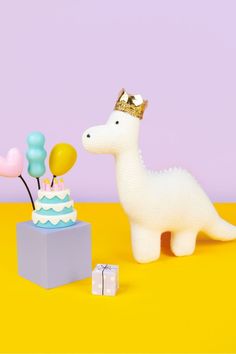 a toy llama with a birthday cake and balloons in front of it on a yellow background