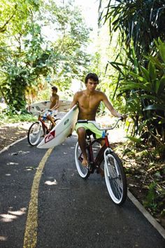 two men riding bikes down a road with surfboards on the front and back wheels