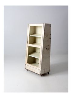 an old white cabinet with shelves on wheels