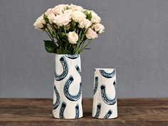 two vases with white roses in them on a wooden table next to each other