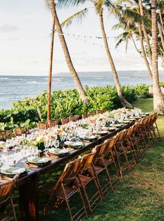 a long table is set up with plates and glasses for an outdoor dinner by the ocean