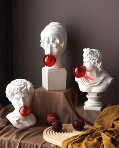 three marble busturines are sitting on a table with grapes and cherries in front of them