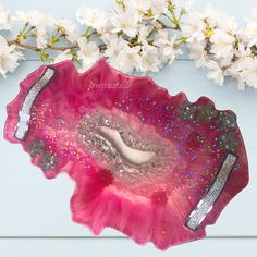 a pink and silver plate with some flowers on it next to a branch of white flowers