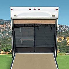 the back end of an rv with its doors open and mountains in the distance behind it