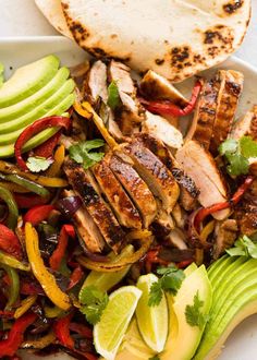 a white plate topped with meat and veggies next to sliced avocado