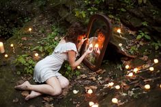 a woman sitting on the ground in front of a mirror with lit candles around it