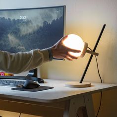 a person holding a light up in front of a computer screen on a desk with a keyboard and mouse