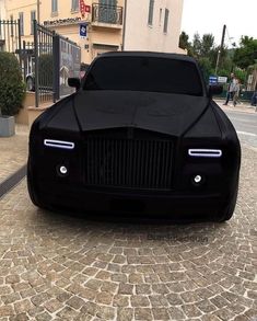 a black rolls royce parked in front of a building on a cobblestone street