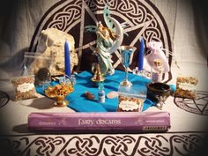 a table topped with books and candles on top of a blue cloth next to an angel statue