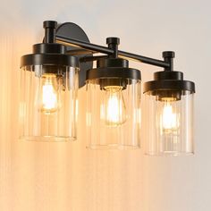 three light bathroom fixture with clear glass shades and black metal fixtures, on a white wall