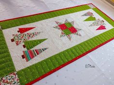 a quilted table runner on top of a white table with red and green trimmings